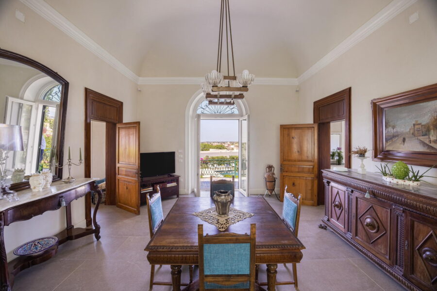 Spacious dining room in Villa Stella, featuring vintage wooden furniture, high ceilings, and a stunning view of the Sicilian countryside.