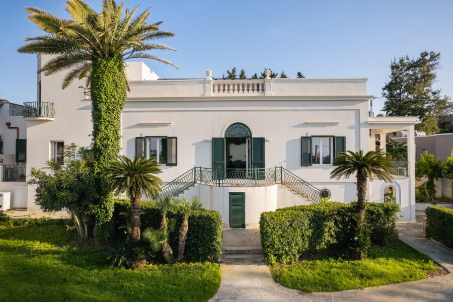 Front view of a luxury Mediterranean villa in Sicily with palm trees and manicured gardens.