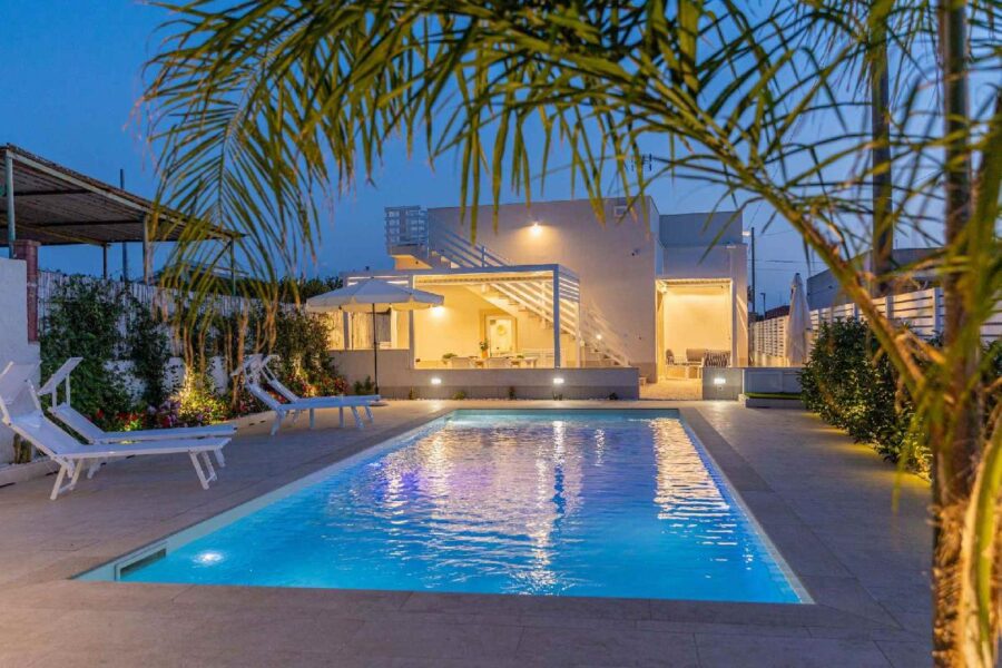 Evening view of Villa Blue Oasis, a luxurious Sicily villa with a private illuminated pool, modern outdoor spaces, and elegant lounge areas.