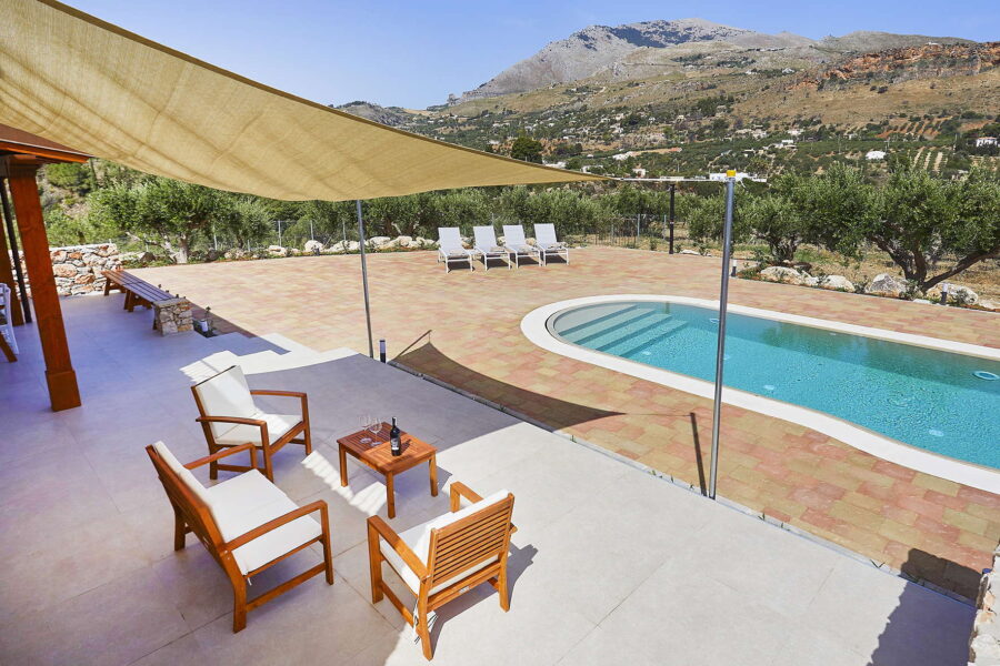 VillaPietraDorata-CastellammareDelGolfoRelaxingPoolsideTerrace-ScentOfSicily Spacious poolside terrace with shaded seating, sun loungers, and panoramic mountain views at Villa Pietra Dorata, Sicily.