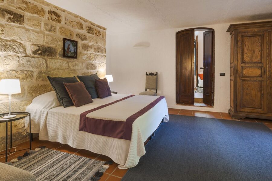 Double bedroom with exposed stone wall, terracotta floor, and classic wooden furniture in Villa Selvira, a beautifully restored Sicily villa with pool.