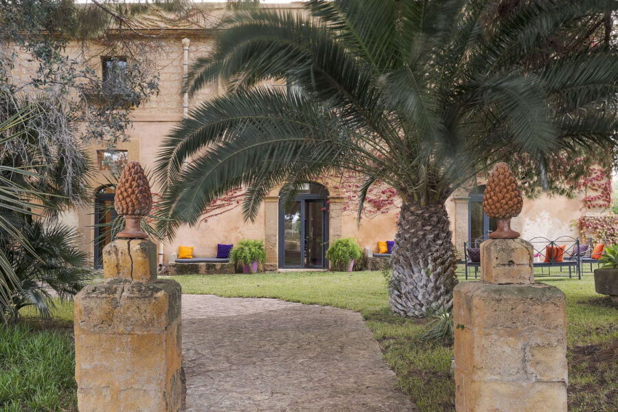 Pathway flanked by stone pillars and palm trees leading to the garden entrance of Villa Selvira, an elegant and private Sicily villa with pool.