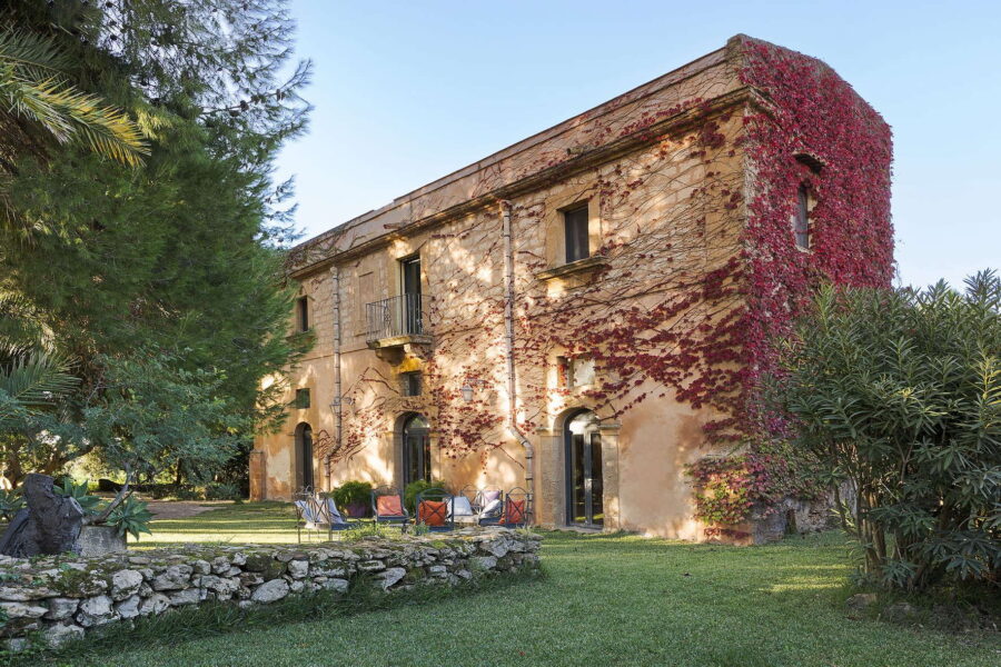 Exterior view of Villa Selvira with sunlit stone walls, red ivy, and outdoor seating area on a lush green lawn – a standout Sicily villa with pool.