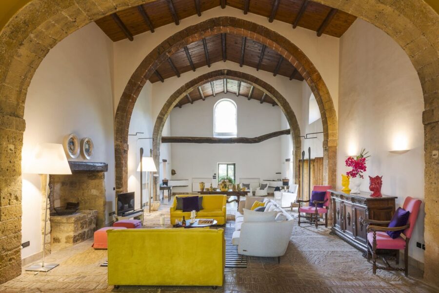 Spacious living room with vaulted ceiling, historic stone arches, colorful modern seating, and rustic flooring in Villa Selvira, a signature Sicily villa with pool.