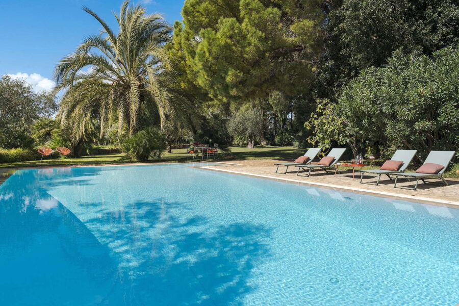 Large turquoise pool framed by palm trees, sun loungers, and lush garden at Villa Selvira, a top-tier Sicily villa with pool.