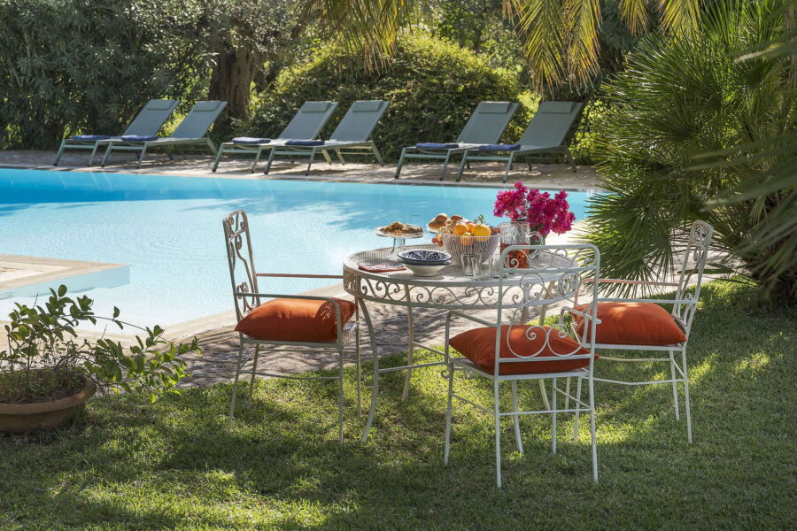 Shaded garden table with orange cushions and fruit platter by the crystal-clear pool at Villa Selvira, one of the most relaxing Sicily villas with pool.